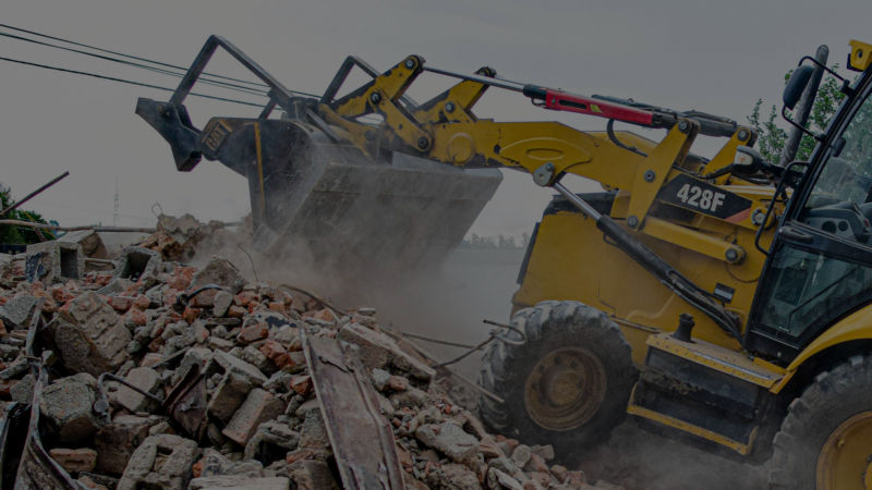 A yellow digger truck climbing a pile of concrete debris