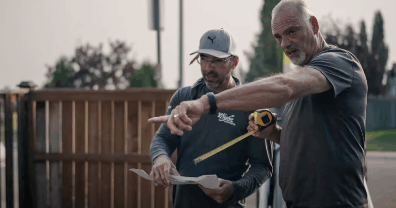 Two landscapers standing together outside, one pointing.