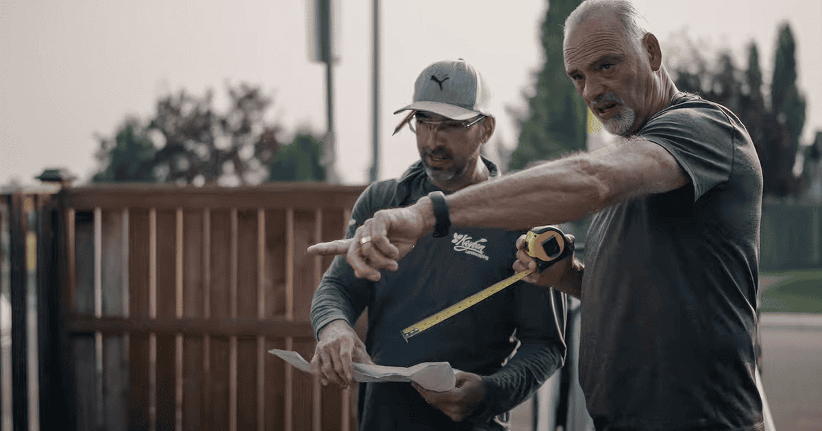 Two landscapers standing together outside, one pointing.